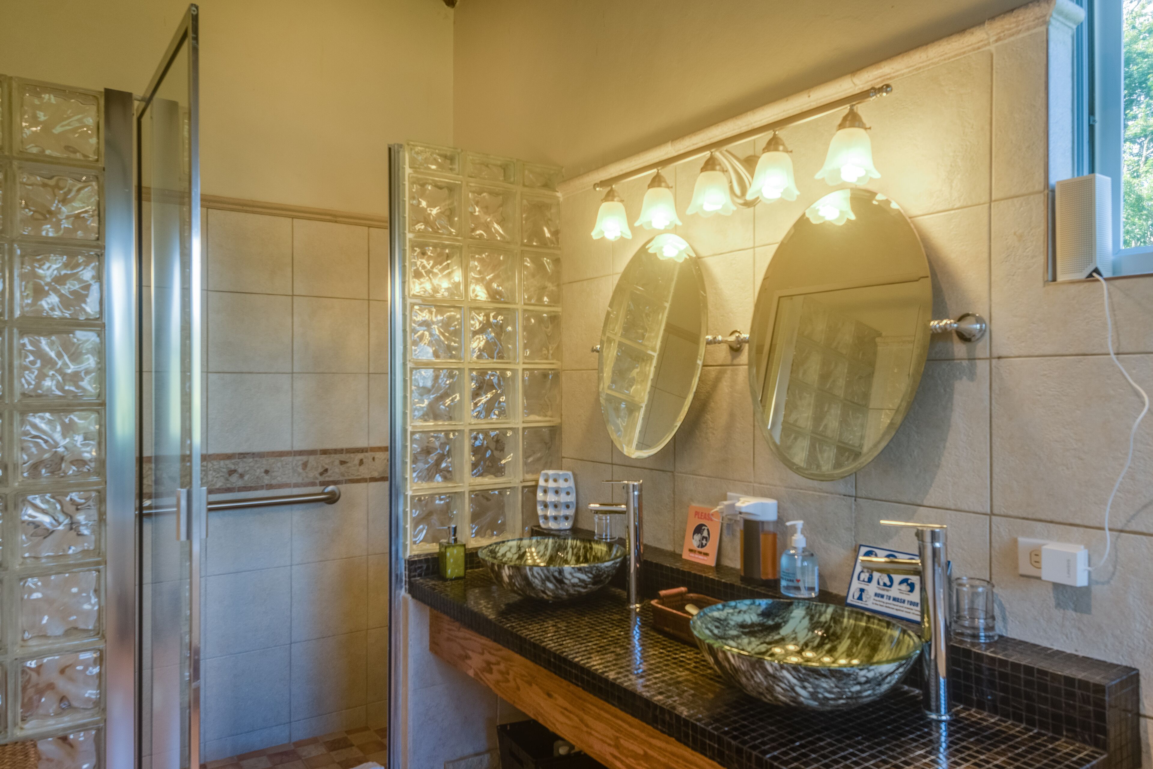 Une salle de bain avec une douche à parois de verre, deux grands miroirs et un lavabo en forme de cuvette.