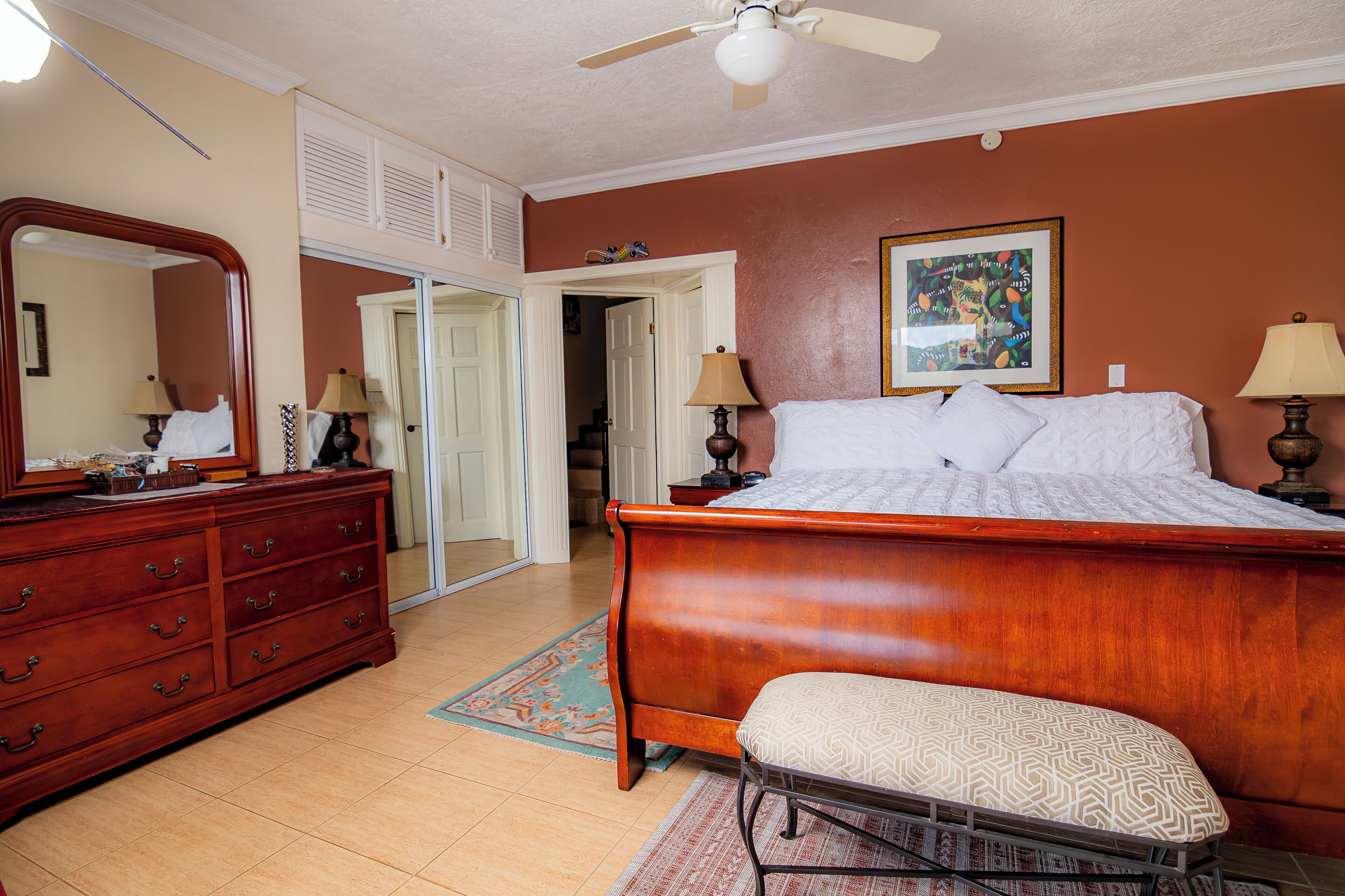 A bedroom with a wooden bed, a bench, a dresser, a mirror, and a ceiling fan.