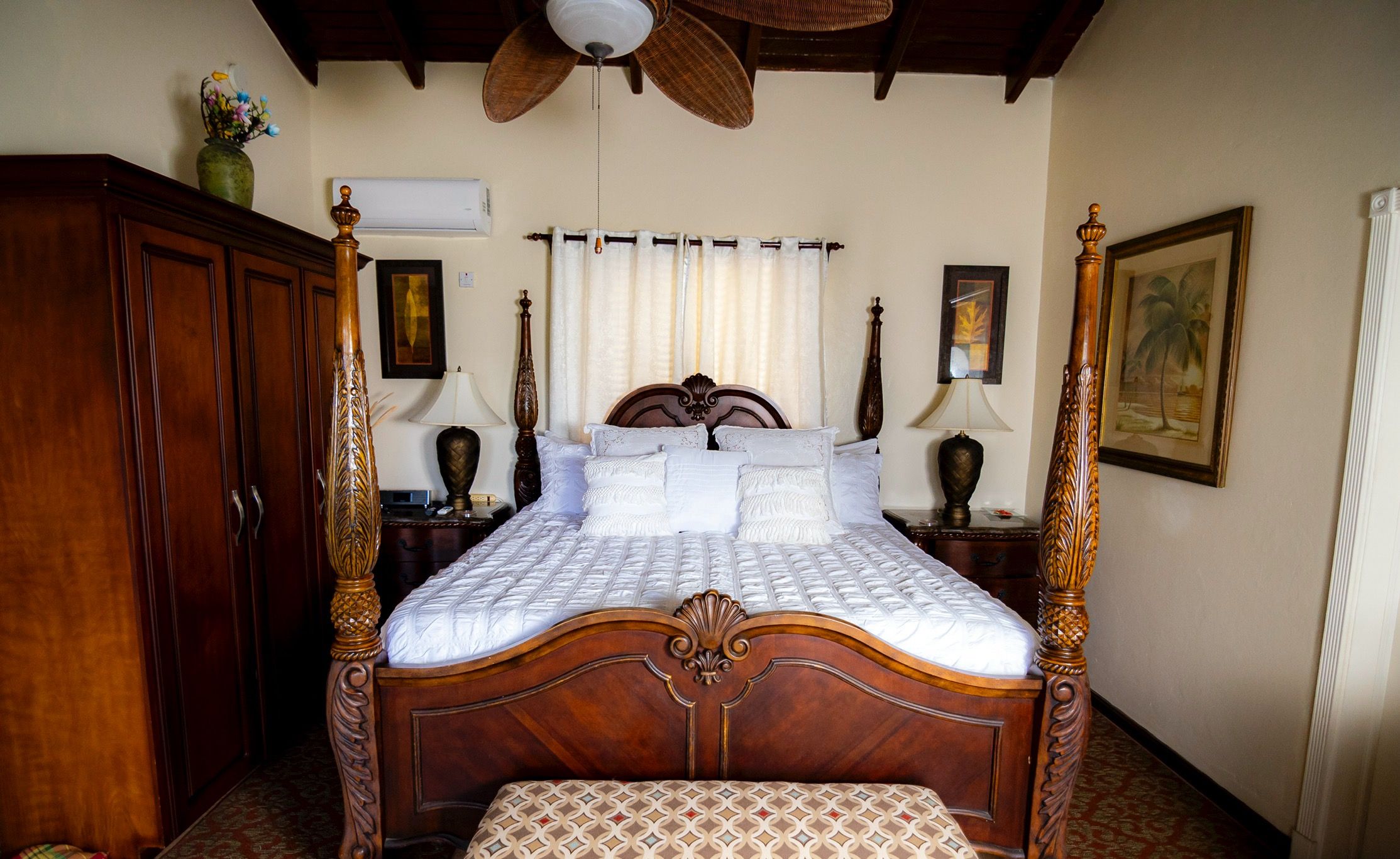 Eine Marigot-Suite mit einem hölzernen Himmelbett, einem Deckenventilator und einem Gemälde an der Wand.