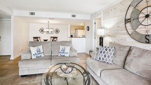 A living room with two sofas, a coffee table, a wall clock, and a large compass decoration. - Bay Views, Walk to Beach, Resort Amenities - Land's End 1-208 (Treasure Island)