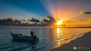 Een zonsondergang boven een rustige zee, met een boot en een persoon die erop staat.