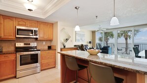 A kitchen with wooden cabinets, stainless steel appliances, a large island with bar stools, and a view of the ocean through large windows.