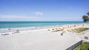 A beach with white sand, clear blue water, and yellow umbrellas.