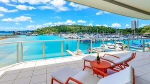 A balcony with two wicker lounge chairs and a table, overlooking a marina with numerous boats and a clear blue sky. - Pavillions Penthouse 25 - Waterfront with private pool, golf buggy and transfers (Hamilton Island)