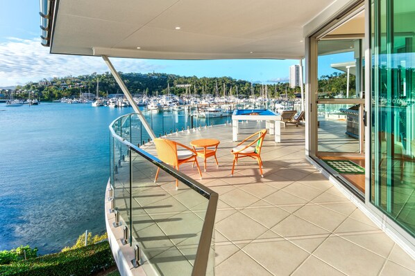 Un balcon équipé d’une table de billard, de chaises et offrant une vue sur une marina remplie de bateaux.