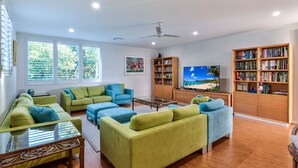 A modern living room with green sofas, a coffee table, a TV, and bookshelves. - Pavillions Penthouse 25 - Waterfront with private pool, golf buggy and transfers (Hamilton Island)