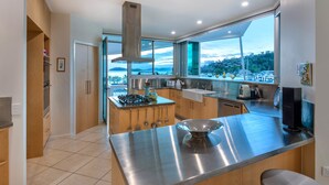 A modern kitchen with a large island, stainless steel appliances, and a view of the marina. - Pavillions Penthouse 25 - Waterfront with private pool, golf buggy and transfers (Hamilton Island)