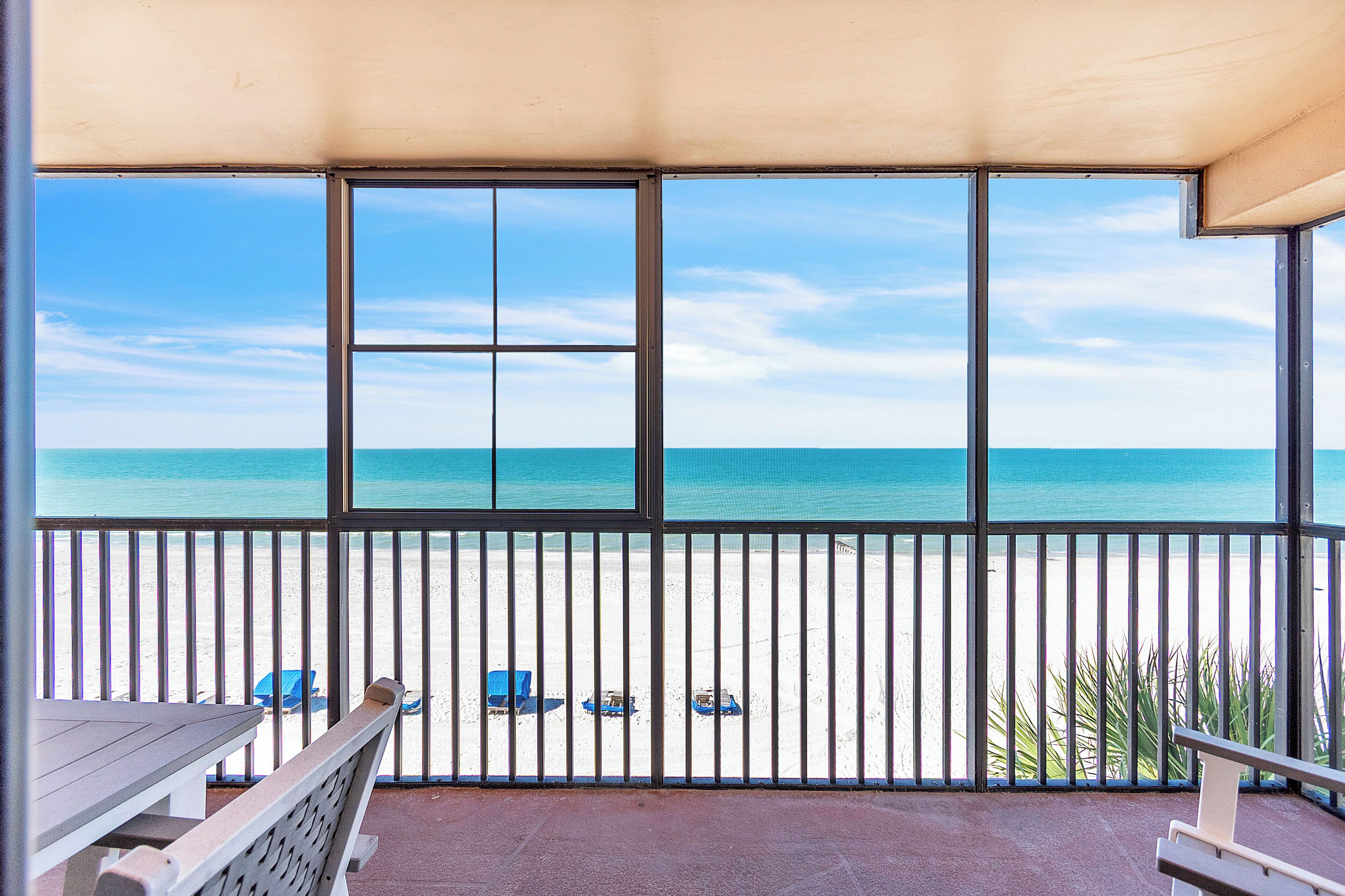 Uma varanda com vista para a praia, uma mesa e duas cadeiras azuis.
