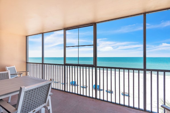 A covered outdoor area with a table and chairs, a view of the beach, and a railing.