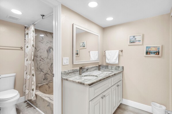 A bathroom with a toilet, shower, vanity with a sink, and a large mirror.