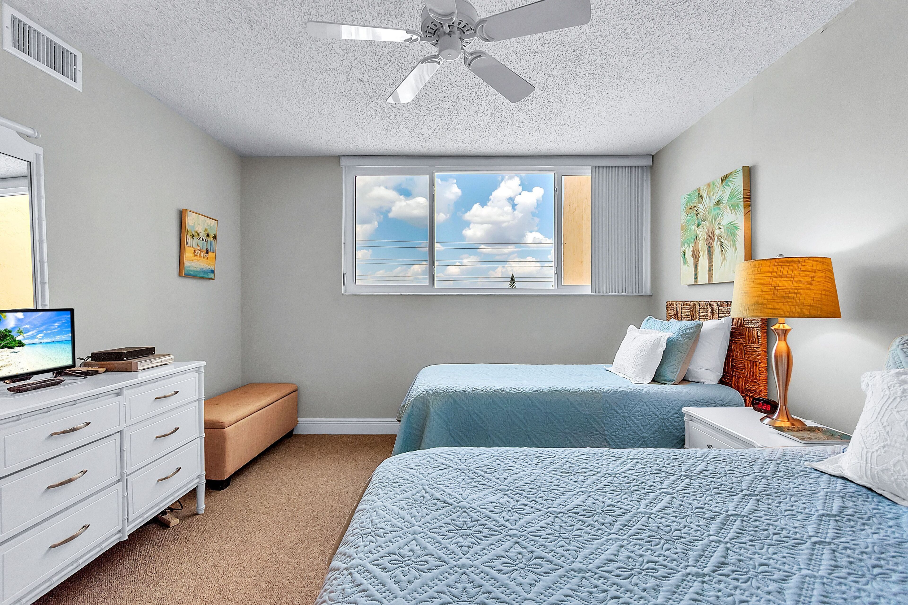 A bedroom with two beds, a ceiling fan, a window with a view, a TV, and a dresser.