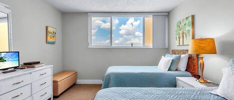 A bedroom with two beds, a ceiling fan, a window with a view, a TV, and a dresser.