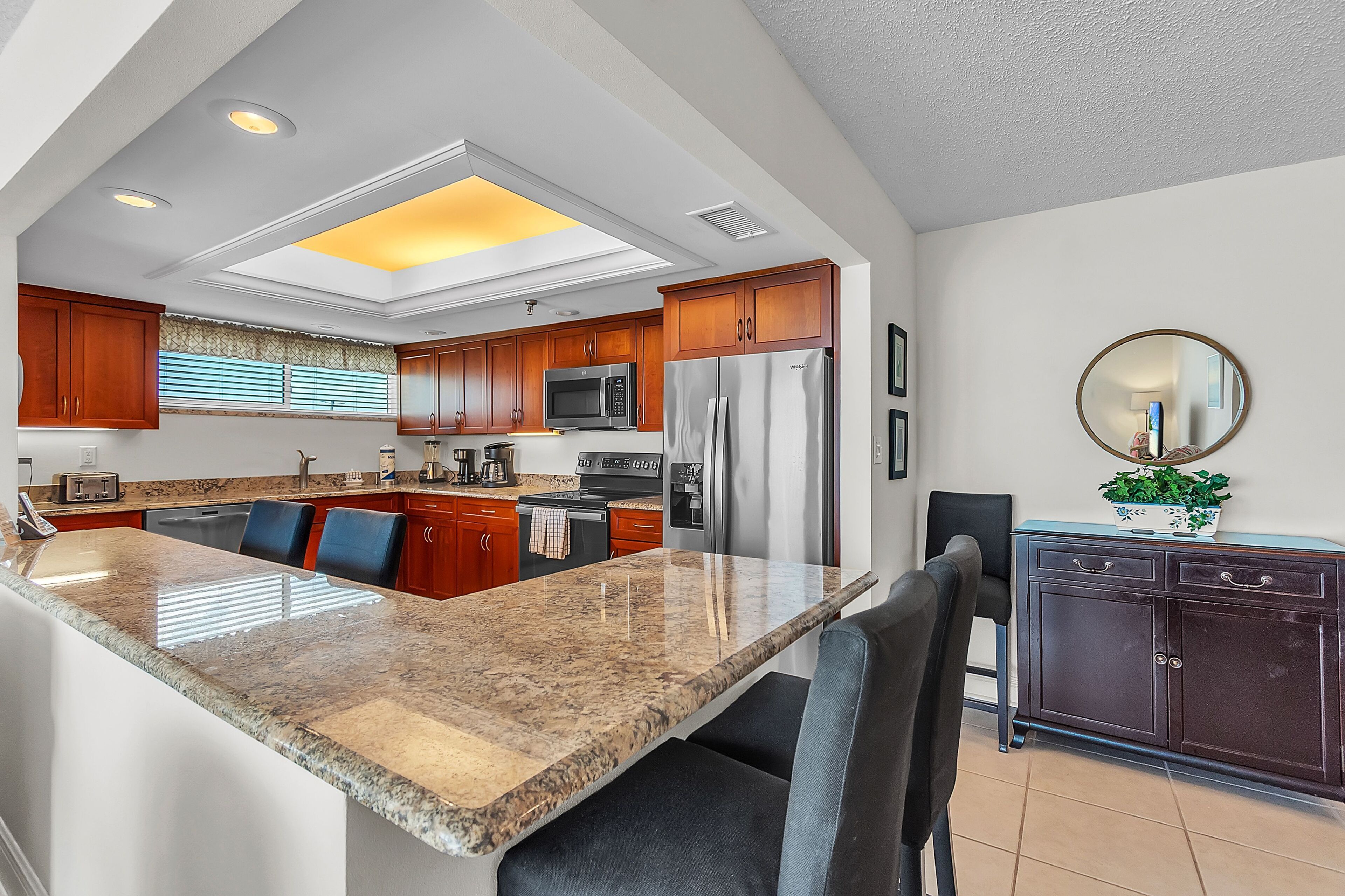 A modern kitchen with granite countertops, wooden cabinets, stainless steel appliances, and a skylight.