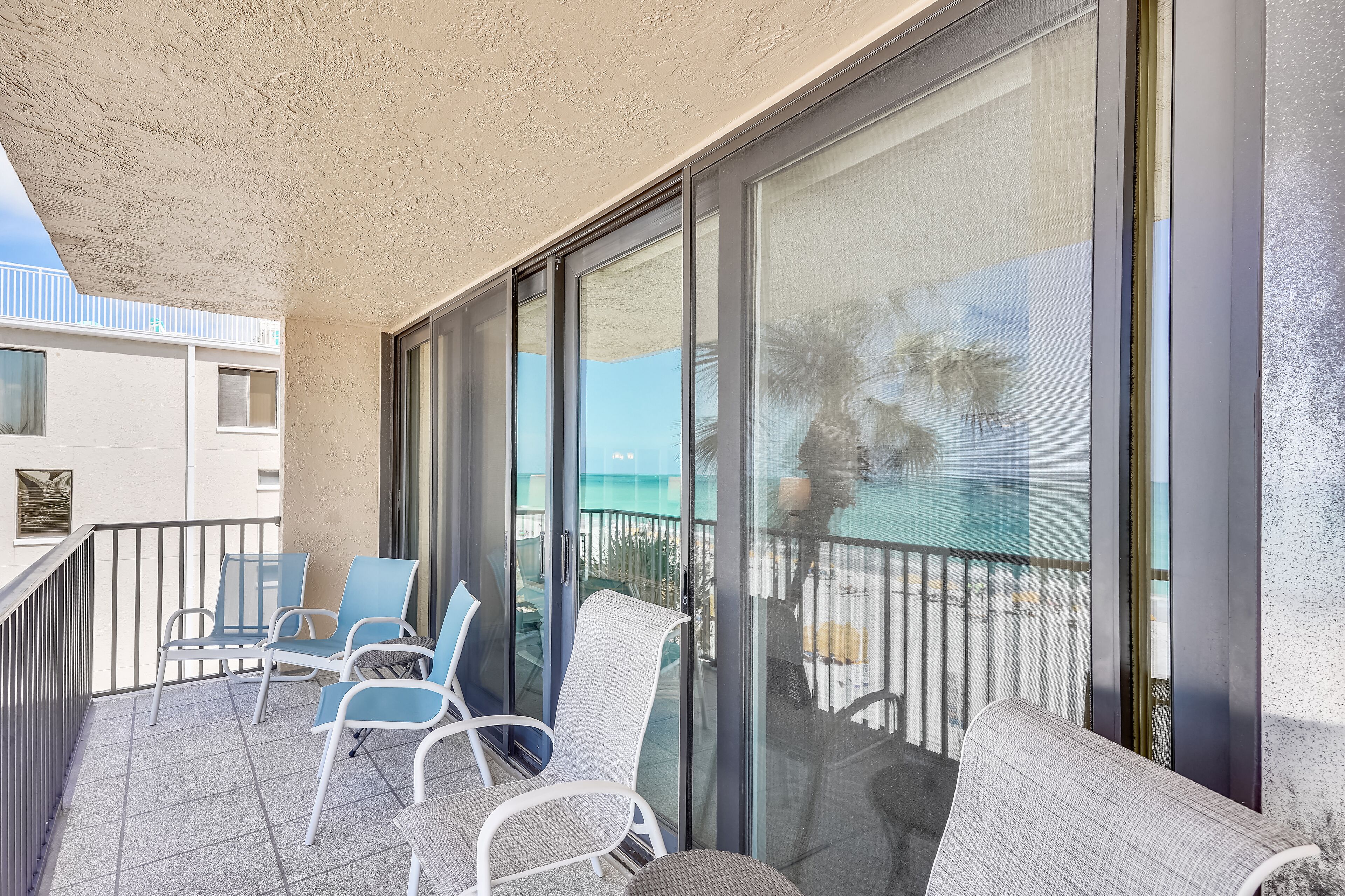 A balcony with chairs and a sofa, a glass door, and a view of the sea.