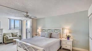 Un dormitorio con cama, mesitas de noche, cómoda, ventana y ventilador de techo.