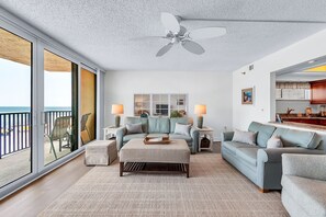 A spacious living room with a large window, a ceiling fan, and a view of the ocean.