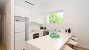 A modern kitchen with white cabinetry, a microwave, a kettle, and a coffee maker.