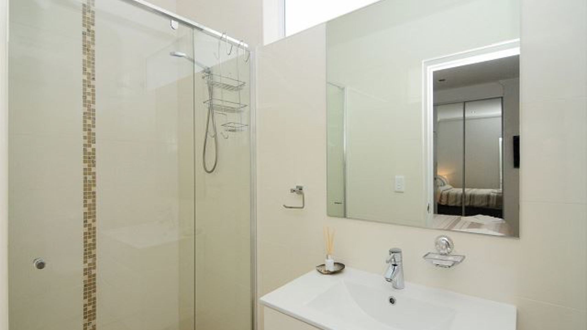 Une salle de bain moderne avec une douche à parois de verre, un lavabo blanc avec un miroir au-dessus et un petit porte-serviettes.