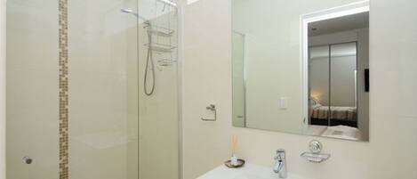 A modern bathroom with a glass shower enclosure, a white sink with a mirror above it, and a small towel rack.