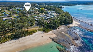 An aerial view of a coastal area with a cluster of houses near the beach, surrounded by greenery and rocky coastline.