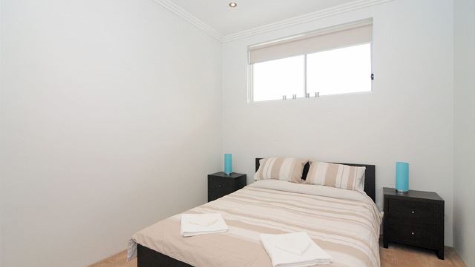 A bedroom with a bed, two bedside tables, a window, and a nightstand.
