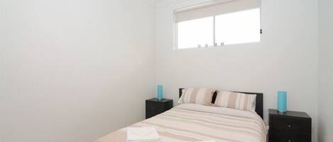 Een slaapkamer met een bed, twee nachtkastjes, een raam en een bedbank.