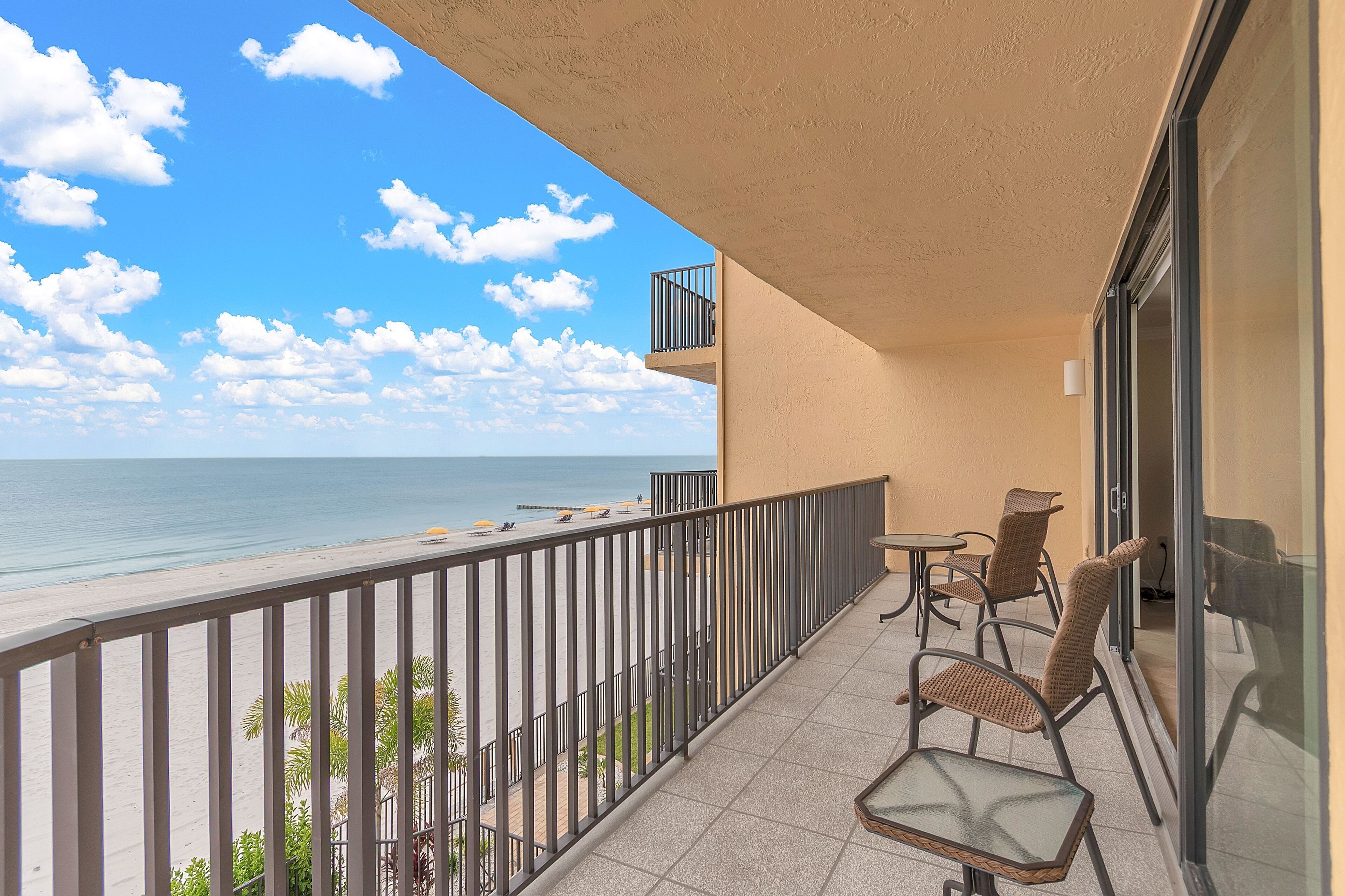 A balcony with a view of the beach, a glass door, and wicker chairs.