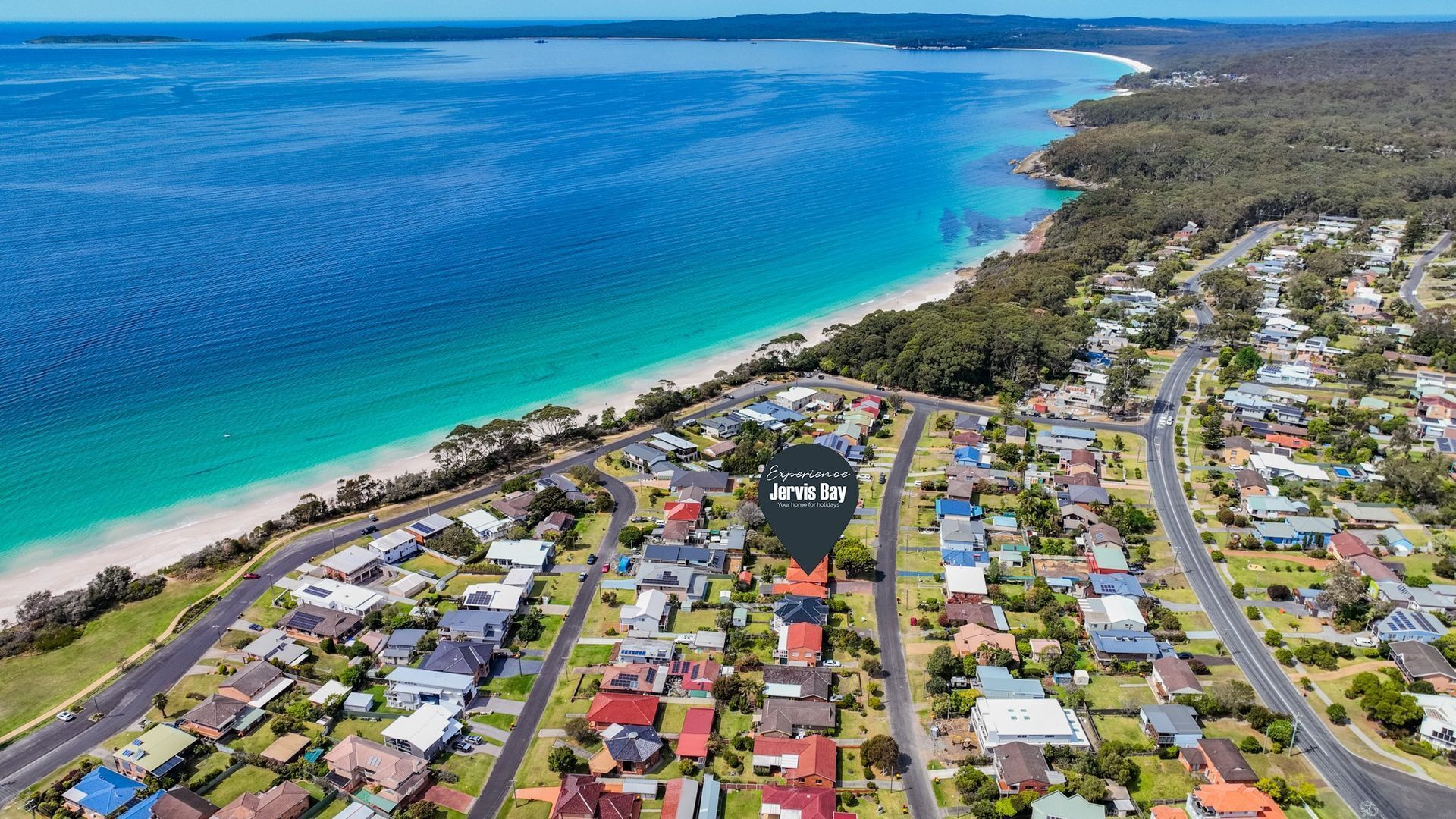 An aerial view of a coastal residential area with houses, roads, and a beach.