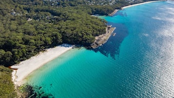 An aerial view of Jervis Bay with a beach, clear turquoise waters, and dense forested areas.