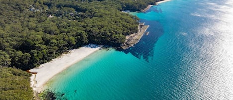 Vista aérea de la bahía Jervis, con una playa, aguas turquesas cristalinas y zonas boscosas densas.