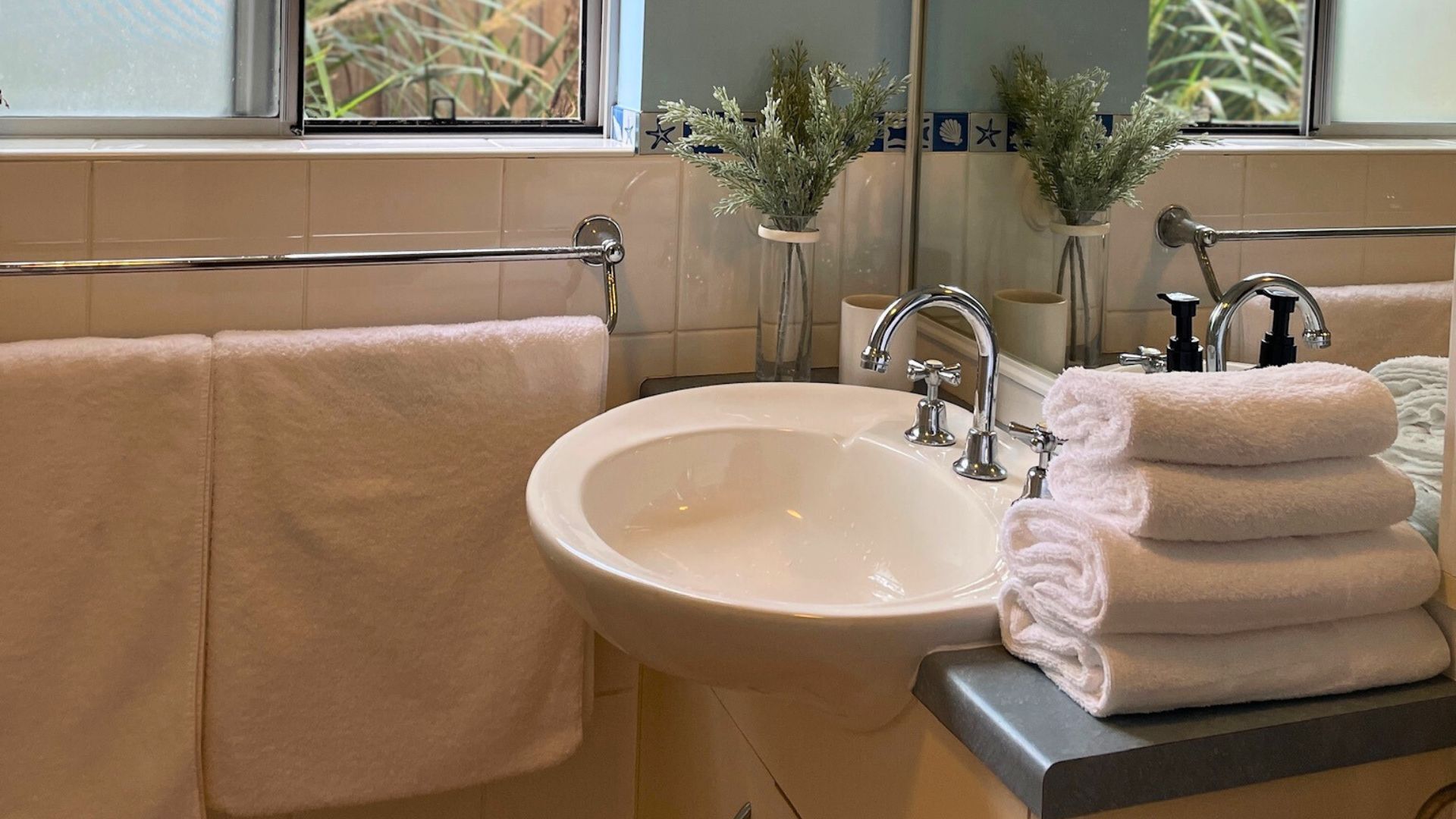 A bathroom with a sink, two towel bars, and two potted plants.