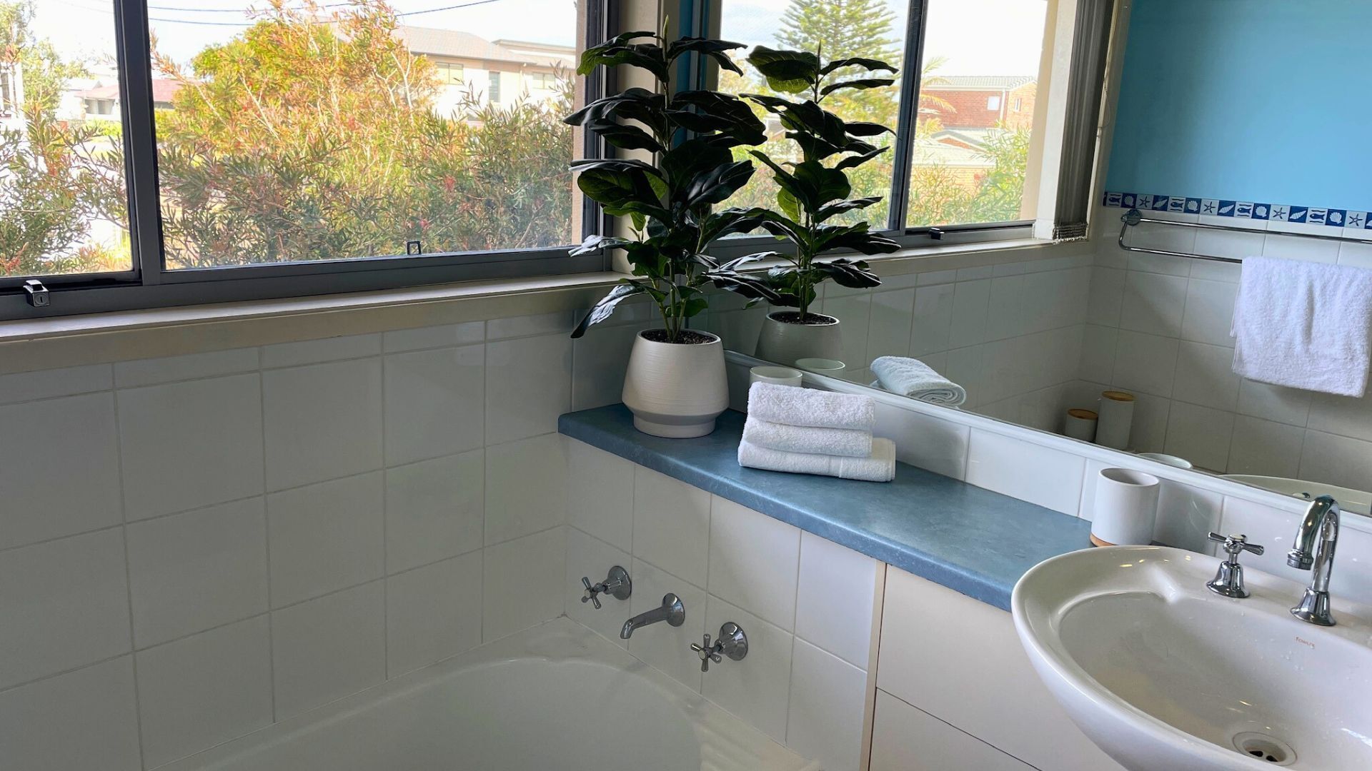 A modern bathroom with a bathtub, a sink, and a window with a view of trees and buildings.