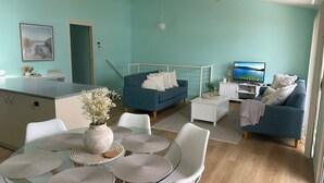 Un salon moderne avec un canapé bleu, un téléviseur et un coin repas doté d’une table en verre.