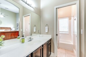 Une salle de bain avec un lavabo blanc, un grand miroir et une baignoire.