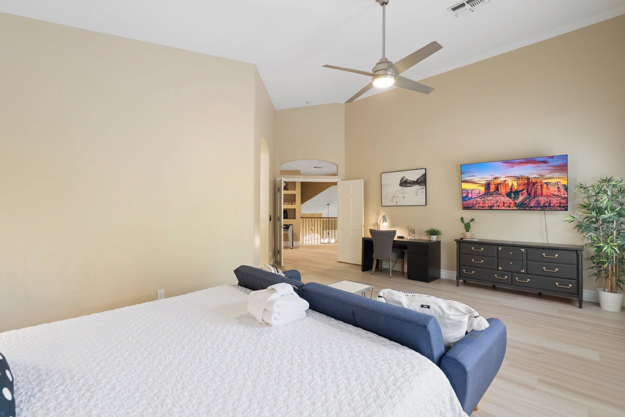 Une chambre à coucher comprenant un lit, un bureau, une chaise, un téléviseur et un ventilateur de plafond.