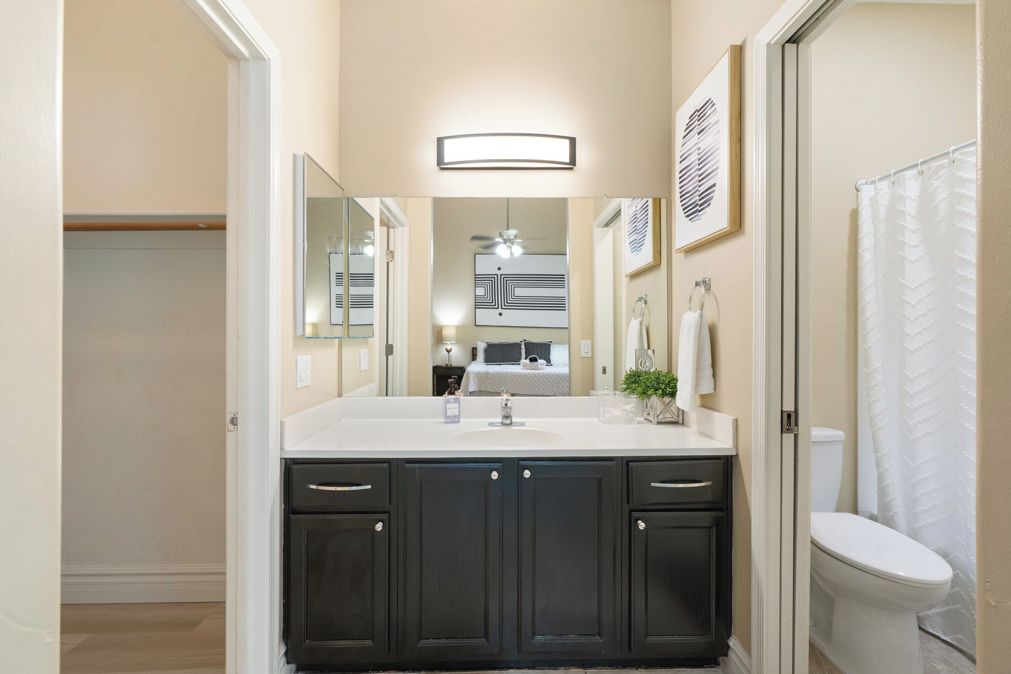 Une salle de bain avec un lavabo blanc, des meubles sombres, un miroir, un ventilateur de plafond et un rideau de douche.