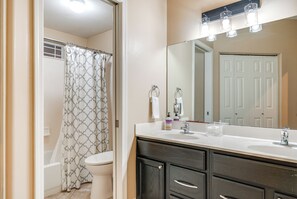 Une salle de bain avec un rideau de douche, des toilettes, un meuble-lavabo avec un miroir et un évier.