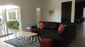A modern living room with a black sectional sofa, red and blue cushions, a white coffee table, and a striped rug. There is a dining area in the background with a black table and chairs. - Bella Vita @ Yarrawonga (Yarrawonga)