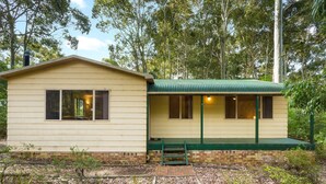 A small, single-story building with a green roof and a brick foundation. It features a porch with a green bench and a small staircase leading up to it. - Beachwood  on  Casey (Mystery Bay)
