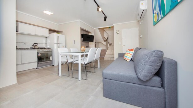 A modern apartment with a dining area, kitchenette, and a gray sofa with a colorful pillow. - 58W Ituzaingó Apartment (Córdoba)