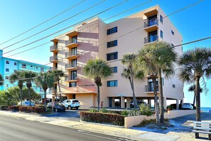 A multi-story hotel with balconies, palm trees, and a parking area.