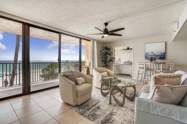 A spacious living area with a balcony overlooking the ocean, furnished with a sofa, armchair, and coffee table.