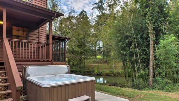 A hot tub on a concrete deck with a wooden deck and stairs leading to a porch.