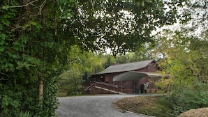 A rustic cabin with a gravel driveway, surrounded by dense foliage.