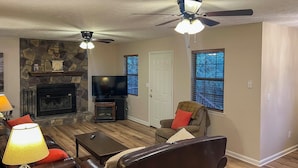 A living room with a stone fireplace, leather sofas, a television, and a ceiling fan.