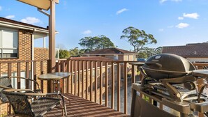 Een terras buiten met een barbecue, een tafel en stoelen.