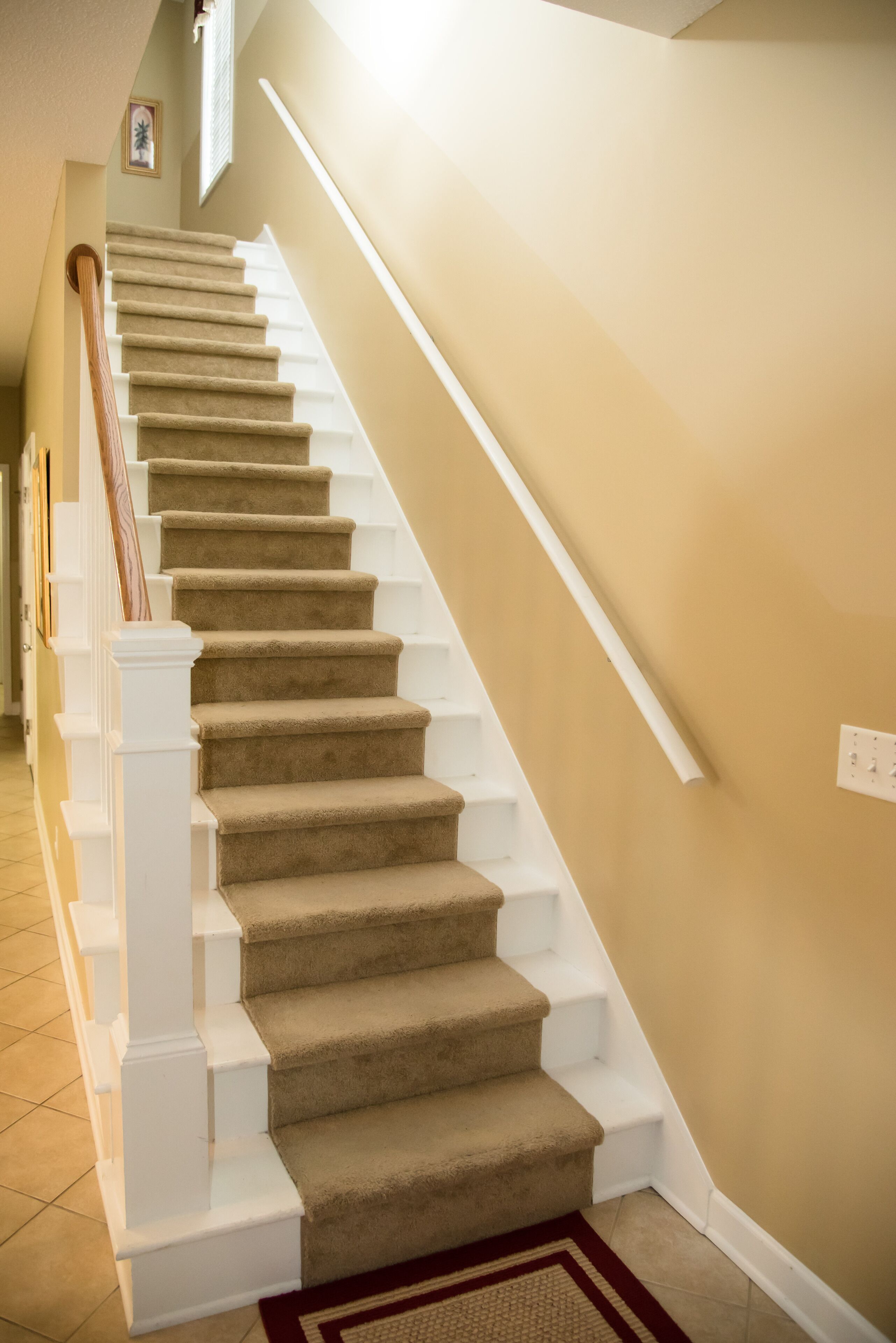 A carpeted staircase with white railings and a red rug at the bottom.