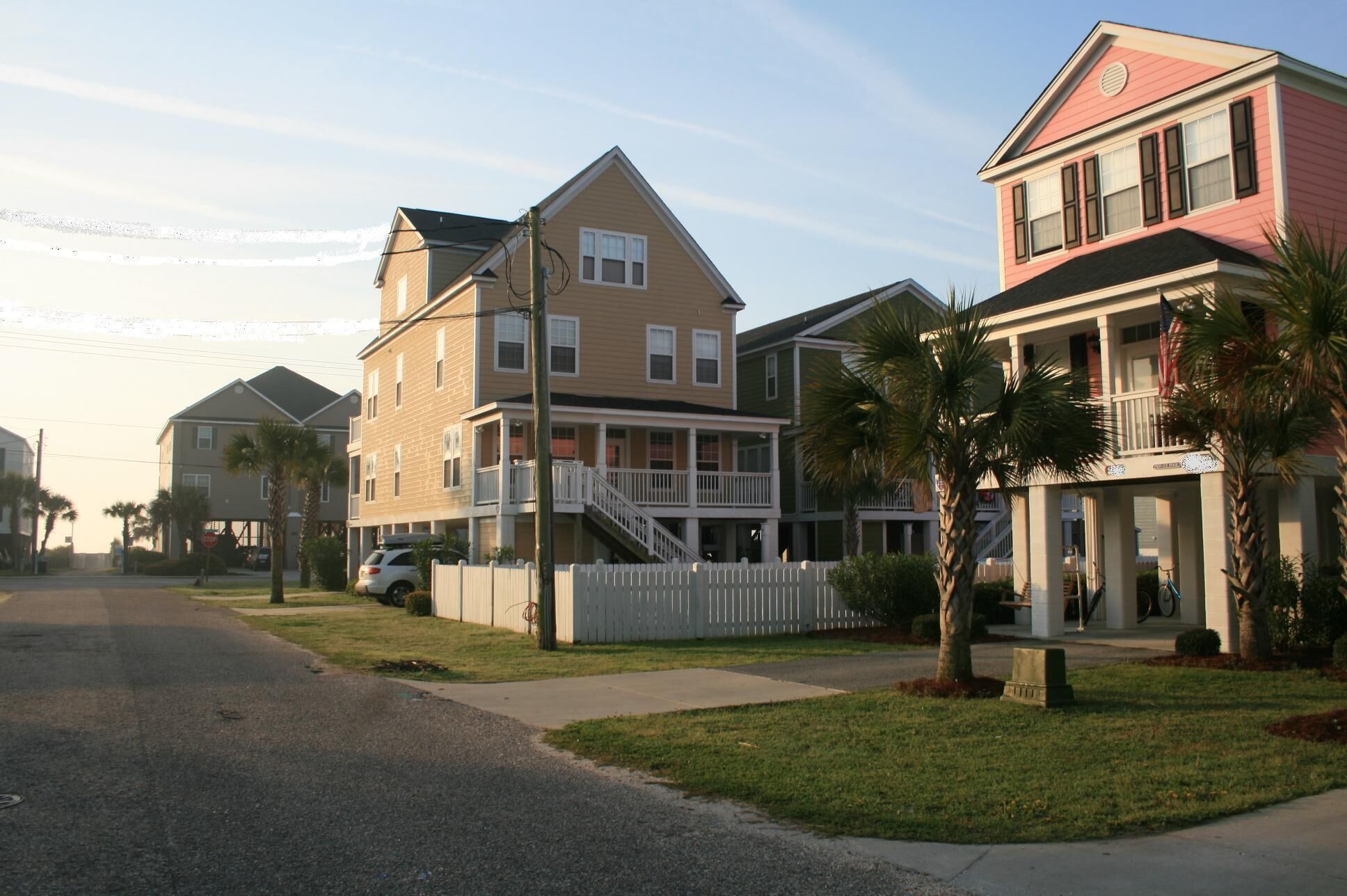 Un quartier résidentiel en bord de mer, avec des maisons à plusieurs étages, une clôture blanche en bois et une voiture garée.