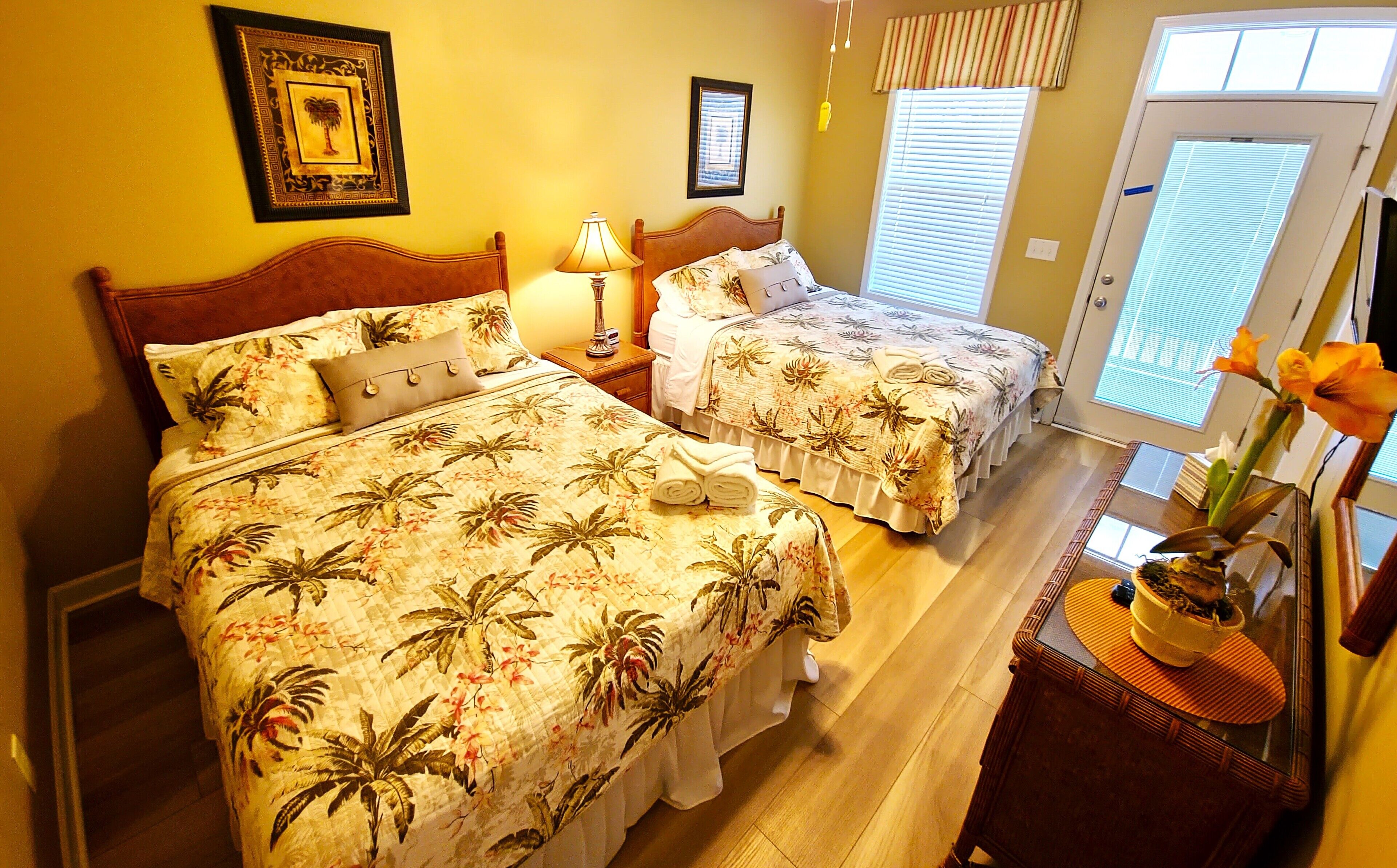 A hotel room with two beds, a wooden headboard, a nightstand with a lamp, and a window with blinds.