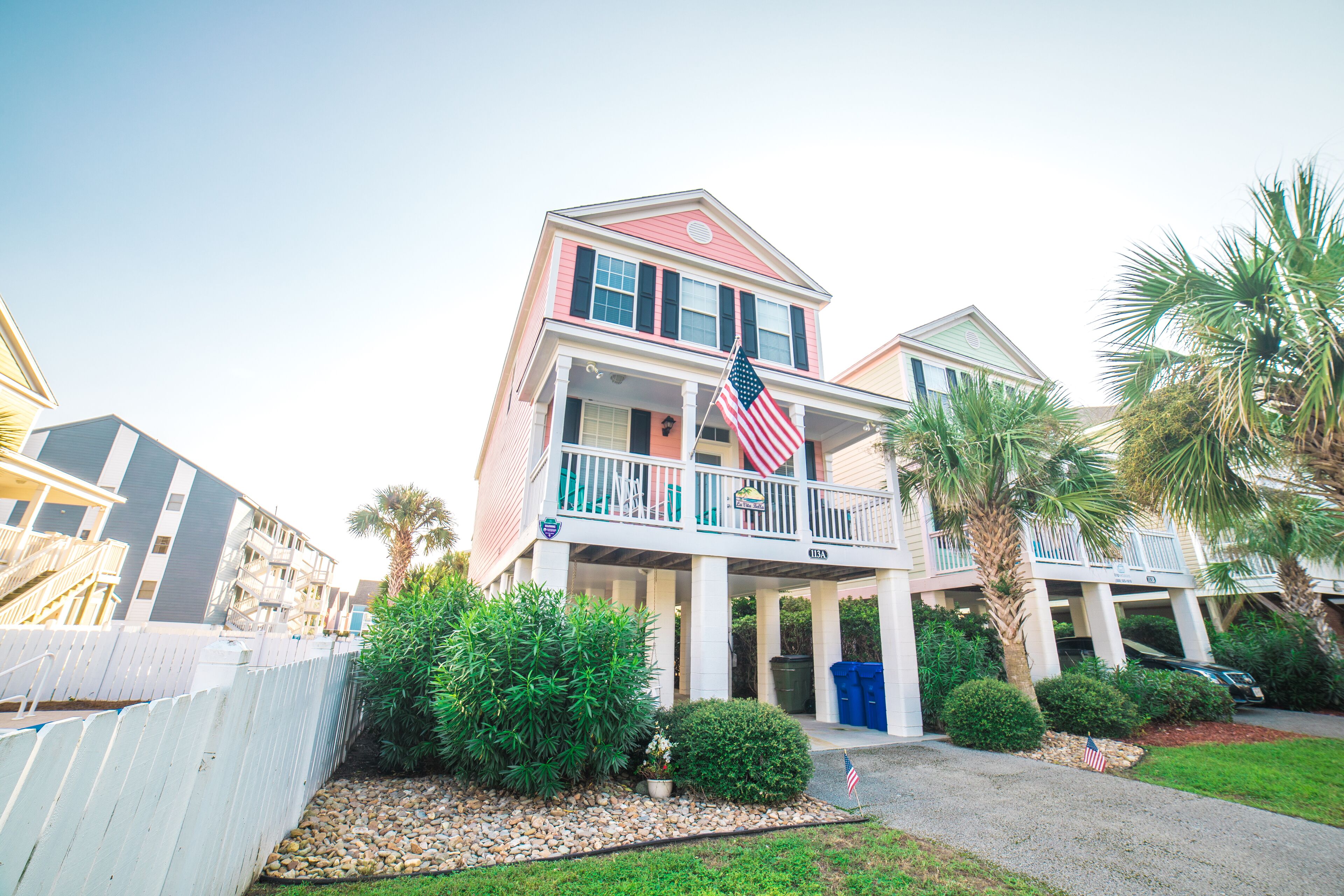 A multi-story building with a balcony, a flag, and a palm tree.